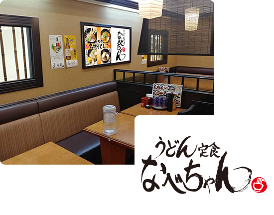 画像:うどん定食なべちゃんの店内、濃い茶色の窓枠があり、竹の仕切りが窓にいくつもついています。店内の壁には、ビールのポスターや、人気のうどんメニューのポスターが貼っています。4人ほど座れるテーブルがいくつもあり、テーブルの上にはお水、テーブルの端にはメニューや調味料が用意されています。