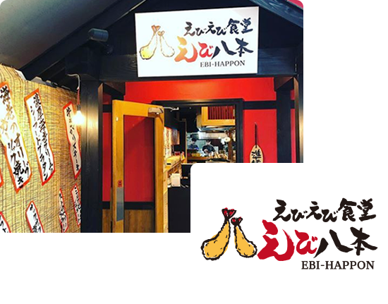 画像:えびえび食堂の入り口、黒い屋根に赤の壁。入り口横の壁には、すだれが掛かっておりメニューの名前が貼られている。